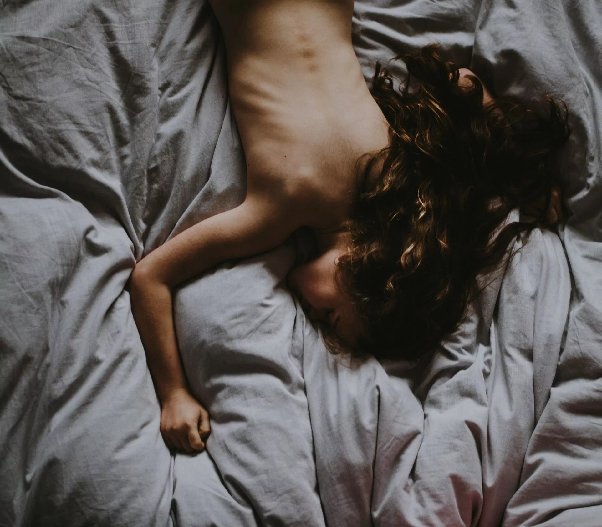 A naked girl laying in gray bedsheets A naked girl laying in gray bedsheets